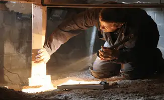 A professional inspecting wooden beams under the floor of a structure in Fort Lauderdale, FL